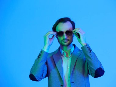 Güneş gözlüklü ve şık gri ceketli zarif genç adam. Stüdyo moda portresi