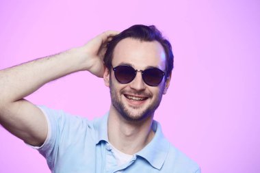 Pembe arka planda güneş gözlüğü takan yakışıklı adamın stüdyo fotoğrafı..