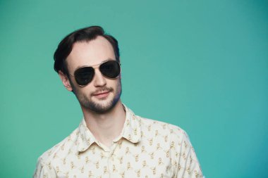 Yeşil arka planda güneş gözlüğü takan yakışıklı adamın stüdyo fotoğrafı..