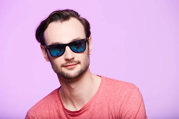 Gros plan portrait de hipster génial portant des lunettes de soleil avec un regard intense à la caméra. Headshot sur fond de studio rose . — Photo