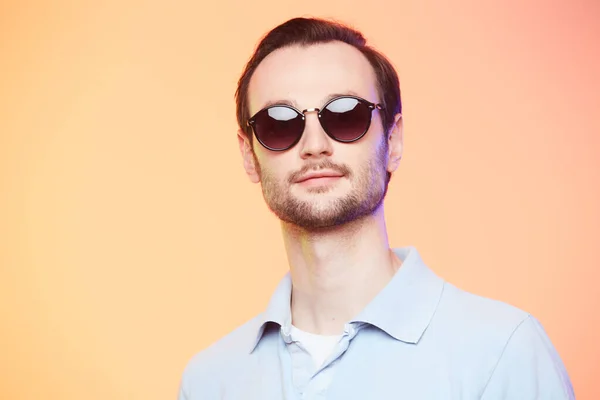Studio shot van knappe man met een zonnebril over oranje achtergrond. — Stockfoto