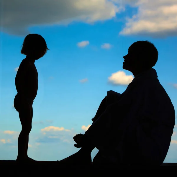 Siluetas de mamá con una hija de 3 años delante de una gran ventana con cielo azul y nubes. Permanecer en casa para la prevención de cuarentena de la pandemia de coronavirus. Autoaislamiento — Foto de Stock