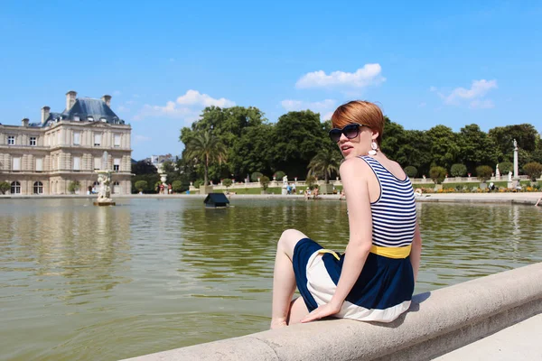 Ung kvinna har en vila på Luxemburg Garden med vackra Luxemburg Palace på bakgrunden under morgonen ljus i Paris — Stockfoto