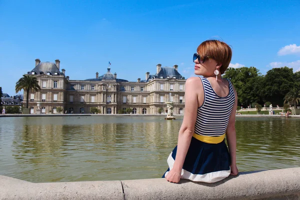 Genç bayan Lüksemburg Bahçesi 'nde dinleniyor. Arkasında güzel Lüksemburg Sarayı var. Sabah vakti Paris' te. — Stok fotoğraf