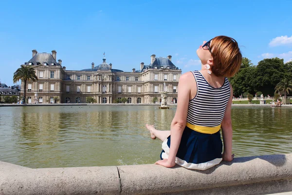 Junge Frau erholt sich im Luxemburger Garten mit dem schönen Luxemburger Palast im Hintergrund im Morgenlicht in Paris — Stockfoto