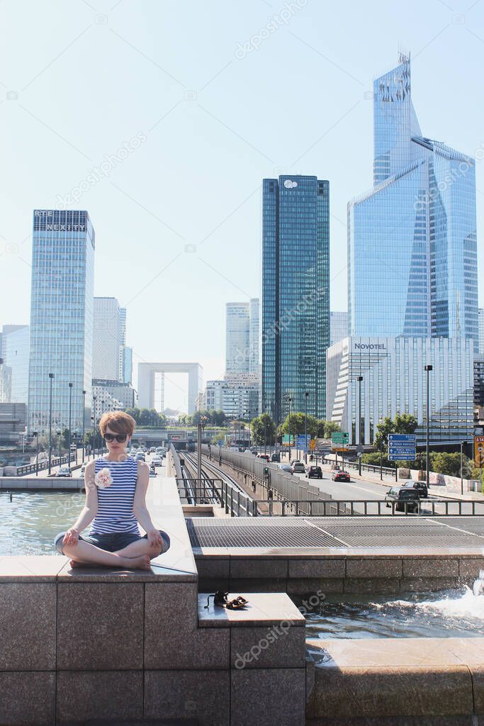 Young woman have a rest at the financial district with beautiful skyscrapers on the background during the morning light in Paris
