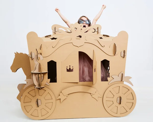 Pequeña princesa en corona 7 años de edad jugar en carruaje de cartón marrón —  Fotos de Stock