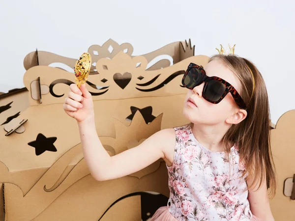 Lovely girl looks in round mirror against carriage made of brown cardboard — Stock Photo, Image