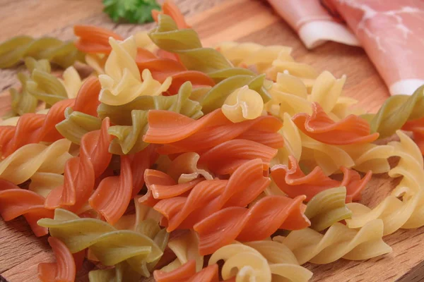 Raw fusilli pasta - three colors and bacon — Stock Photo, Image