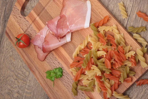 Raw fusilli pasta - three colors and bacon — Stock Photo, Image