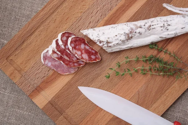 Salami slicing with thyme on board — Stock Photo, Image