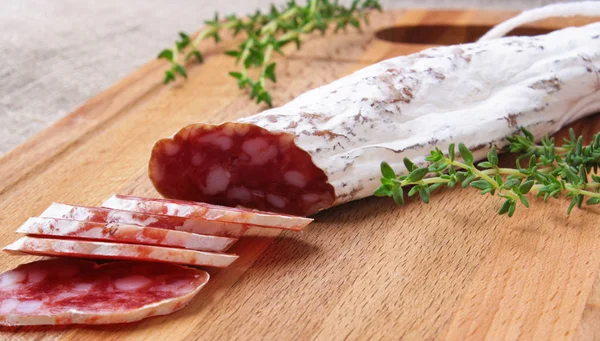 Salami slicing with thyme on board — Stock Photo, Image