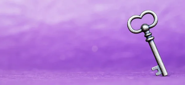 Escape room concept. Vintage key on purple background, web banner with text copy space.