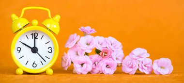 Yaz konsepti, sarı alarm saati ve turuncu arka planda pembe çiçekler. Web pankartı, boşluğu kopyala.