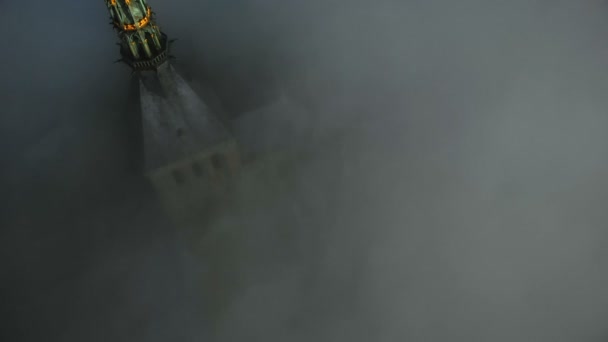 黒い霧の流れの上にあるモンサンミシェル要塞修道院の尖塔の上に金色の像の周りを飛行する映画撮影ドローン — ストック動画