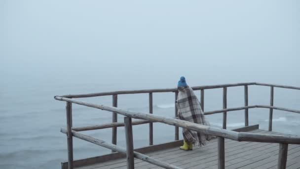 vue arrière de la petite fille en bottes en caoutchouc et plaid debout sur une jetée en bois près de la mer seul enfant dans le brouillard jour venteux 