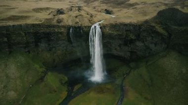 Helikopter, Seljalandsfoss şelalesinden uzaklaşıyor. Sarsıntılı su akıntıları İzlanda 'daki dağdan düşüyor.