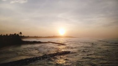 İnanılmaz günbatımı okyanus kıyısında uçan insansız hava aracı dalgaların üzerinde kıyıya ulaşıyor.