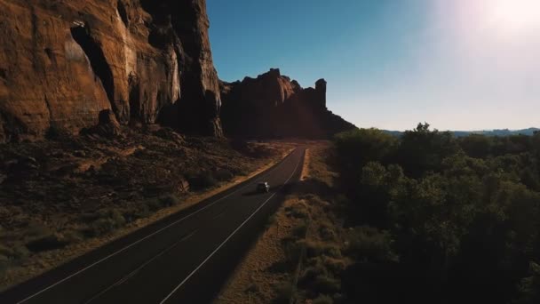 ドローン カメラに続く米国で夕日に息をのむの急峻な峡谷の尾根近く小さな砂漠高速道路道路に沿って運転車 — ストック動画