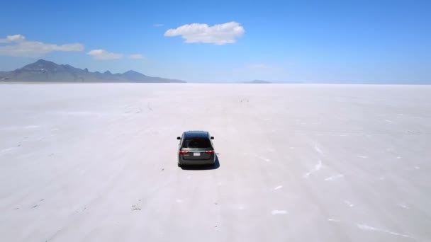 次の息をのむボンネビル塩湖砂漠の真ん中で山に向かって銀ミニバン車ドローン — ストック動画