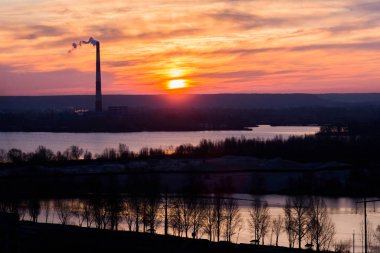  Portakal rengi günbatımı. Fabrikadaki bir baca dumanın içinden güzel bir şafak ve aşağıdaki bir göl arasında geldiği.
