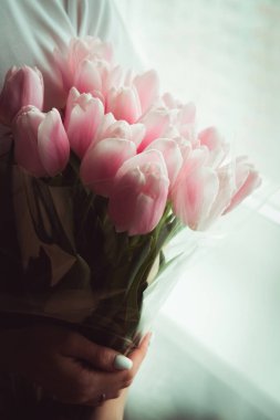 Pembe laleler el ele tutuşur kız pencerenin önünde durur. Bir kızın ellerinde bir buket çiçek. Kız pencerede duruyor ve elinde bir buket pembe lale tutuyor. Tatil. Sevgililer Günü.