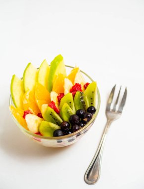 Beyaz arka planda şeffaf cam tabakta meyve salatası. Beyaz arka planda metal çatallı taze meyve salatası.