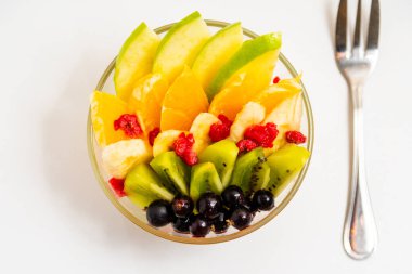 Beyaz arka planda şeffaf cam tabakta meyve salatası. Beyaz arka planda metal çatallı taze meyve salatası.