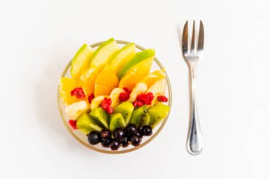 Beyaz arka planda şeffaf cam tabakta meyve salatası. Beyaz arka planda metal çatallı taze meyve salatası.