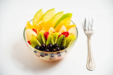 Beyaz arka planda şeffaf cam tabakta meyve salatası. Beyaz arka planda metal çatallı taze meyve salatası.