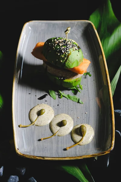 vegan  avocado burger on a black background, fast food, hamburger. Vegan big burger with salmon served on  gray plate