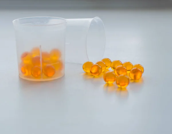 Cápsulas de óleo de peixe em copo de medição na mesa médica branca — Fotografia de Stock