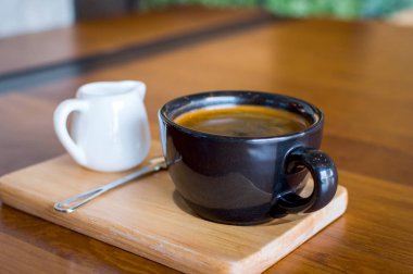 Koyu siyah mavi kahve fincanı americano kahve, kaşık ve süt kabı bir ahşap stand ile