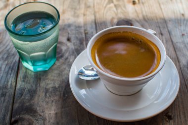 Bir bardak su bir tarafta açık havada ahşap bir masa ile bir beyaz porselen fincan güçlü ve koyu kahve servis