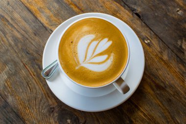 Kahverengi ahşap masada kapuçino bardağı