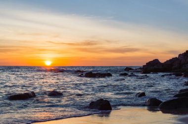 Gündoğumu veya günbatımı turuncu gökyüzü ile tropikal plaj deniz manzarası üzerinde