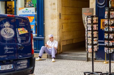Bir aşçı ya da sokakta bir mola sırasında otururken akıllı telefon kullanarak bir kafe işçi. Hareket eden smartphone app mesaj sms mesajı kullanarak tutan genç adam. Fransa, Paris, 02 Ekim 2014