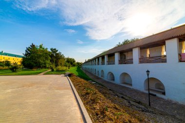 Avlunun beyaz taş duvarı, geniş kemerleri ve yol boyunca ahşap bir çatısı var. Bulutlu havalarda ve mavi bulutlarla kaplı. Tarihsel ve mimari kompleks Astrakhan Kremlin, Rusya