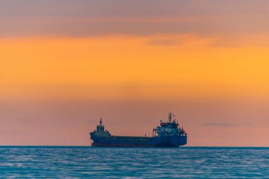 Kargo gemisi altın bir gün batımında ya da gün doğumunda denize açılacak. Güneş batarken ya da doğarken okyanus sevkiyatı. Doğadaki uyum ve güzellik. Huzurlu deniz manzarası.