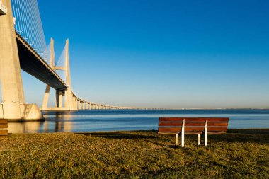 Köprüye tepeden bakan gün batımı ve ön planda bir bank.