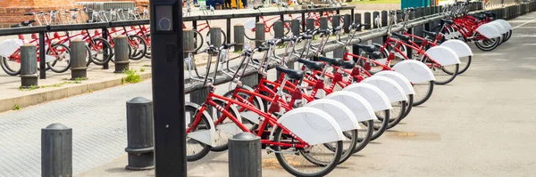 Many red bicycles - City bikes are neatly lined up and ready for rent. Image showing detail and is mainly red colored.