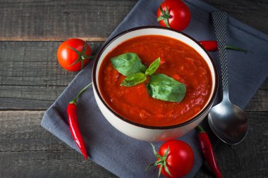 Ekşi krema sos, peynir, fesleğen ve ahşap zemin üzerine kırmızı biber biber domates çorbası. Sağlıklı, vegan ve diyet öğle ve akşam yemeği kavramı.