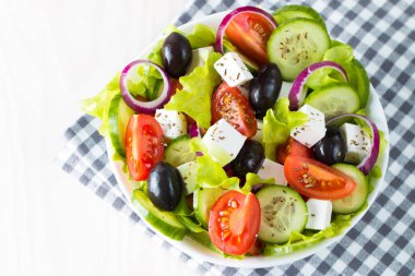 Kiraz domates, ruccola, roka, beyaz peynir, zeytin, salatalık, soğan ve baharat taze Yunan salatası yaptı. Sezar salatası ahşap arka plan üzerinde beyaz bir kase. Sağlıklı organik beslenme gıda kavramı.