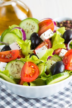 Kiraz domates, ruccola, roka, beyaz peynir, zeytin, salatalık, soğan ve baharat taze Yunan salatası yaptı. Sezar salatası ahşap arka plan üzerinde beyaz bir kase. Sağlıklı organik beslenme gıda kavramı.