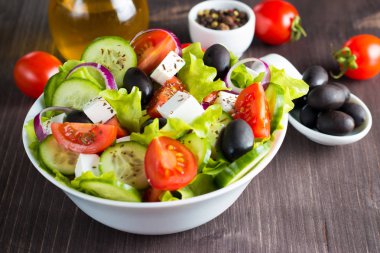 Kiraz domates, ruccola, roka, beyaz peynir, zeytin, salatalık, soğan ve baharat taze Yunan salatası yaptı. Sezar salatası ahşap arka plan üzerinde beyaz bir kase. Sağlıklı organik beslenme gıda kavramı.