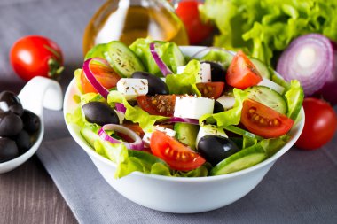 Kiraz domates, ruccola, roka, beyaz peynir, zeytin, salatalık, soğan ve baharat taze Yunan salatası yaptı. Sezar salatası ahşap arka plan üzerinde beyaz bir kase. Sağlıklı organik beslenme gıda kavramı.