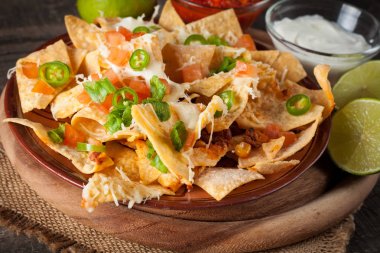 Corn Mexican nachos with beef, jalapeno, cheese, pepper, olives and chili con carne on a wooden background. Lime, Ketchup, sour cream and mayonnaise souce seasoning. clipart