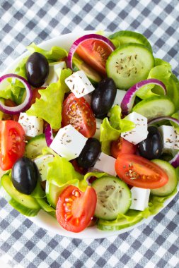 Kiraz domates, ruccola, roka, beyaz peynir, zeytin, salatalık, soğan ve baharat taze Yunan salatası yaptı. Sezar salatası ahşap arka plan üzerinde beyaz bir kase. Sağlıklı organik beslenme gıda kavramı.