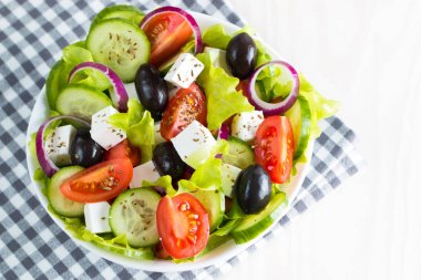 Kiraz domates, ruccola, roka, beyaz peynir, zeytin, salatalık, soğan ve baharat taze Yunan salatası yaptı. Sezar salatası ahşap arka plan üzerinde beyaz bir kase. Sağlıklı organik beslenme gıda kavramı.