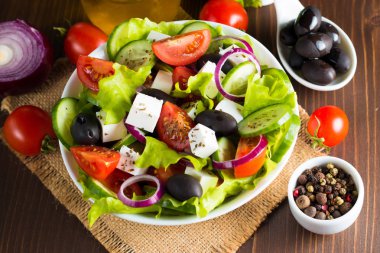 Kiraz domates, ruccola, roka, beyaz peynir, zeytin, salatalık, soğan ve baharat taze Yunan salatası yaptı. Sezar salatası ahşap arka plan üzerinde beyaz bir kase. Sağlıklı organik beslenme gıda kavramı.